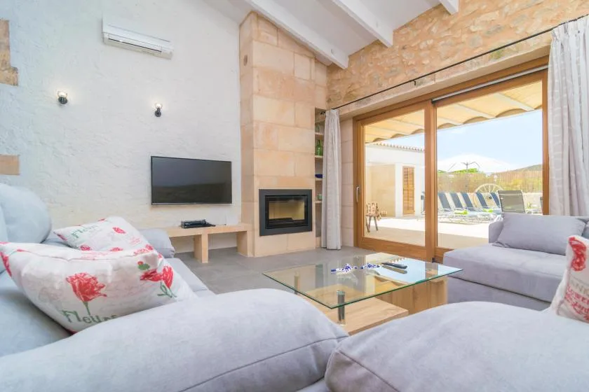 Una sala luminosa con asientos, un televisor y puertas de vidrio que dan a un patio.