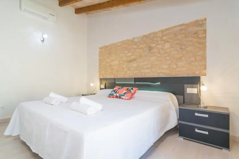Un dormitorio con una cama grande, ropa de cama blanca y una pared decorativa de piedra.