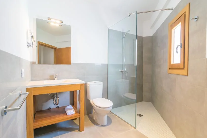 Un baño con mueble de madera, inodoro y ducha de vidrio.