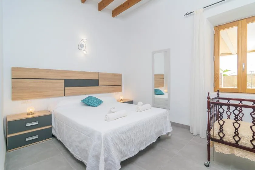 Un dormitorio luminoso con una cama, mesitas de noche y una ventana con marco de madera.