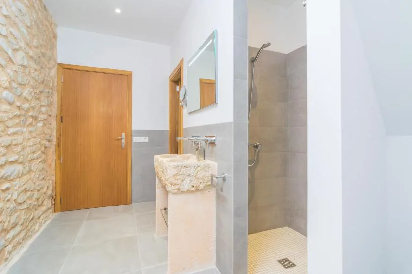 Un baño luminoso con un lavabo de piedra y una ducha abierta.