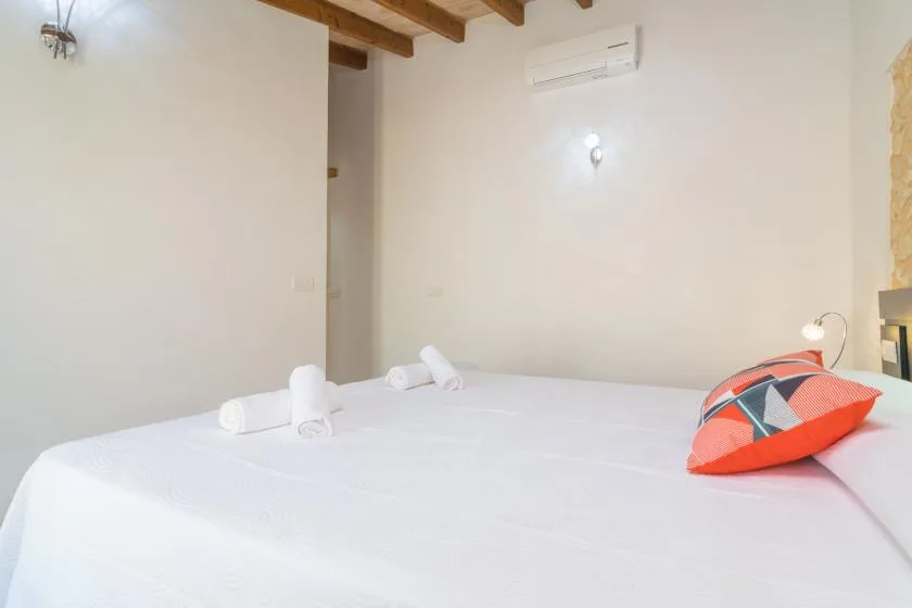 Un dormitorio con una cama blanca, toallas dobladas y un cojín colorido.