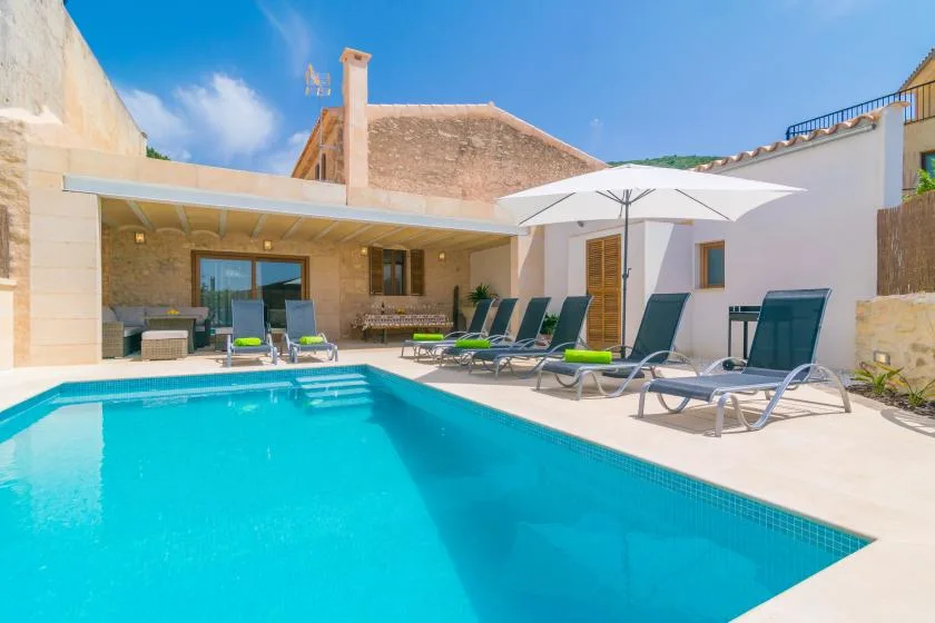 Una piscina al aire libre junto a un patio soleado con asientos reclinables.