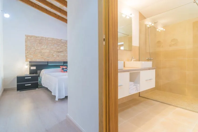 Se ven un dormitorio y un baño contiguo, con una cama y un mueble de lavabo.