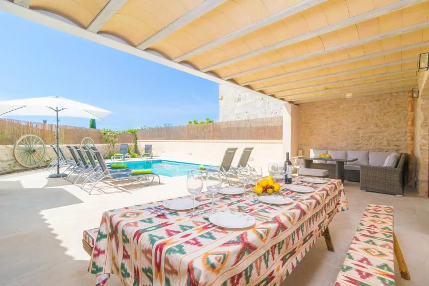 Una zona de comedor cubierta se abre a una piscina, con un mantel estampado en primer plano.