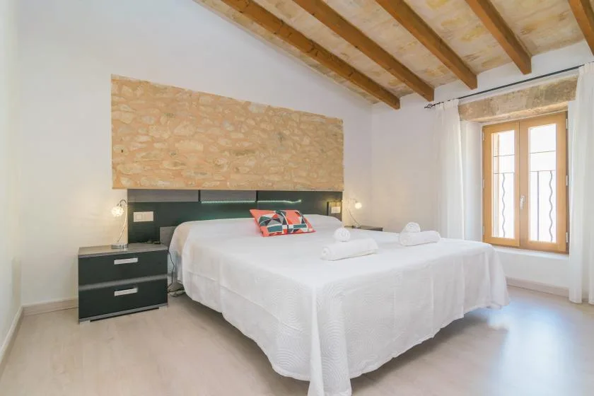 Un dormitorio luminoso con una cama grande bajo vigas de madera expuestas.