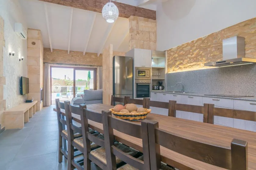 Comedor y cocina de planta abierta con una larga mesa de madera y grandes ventanales.