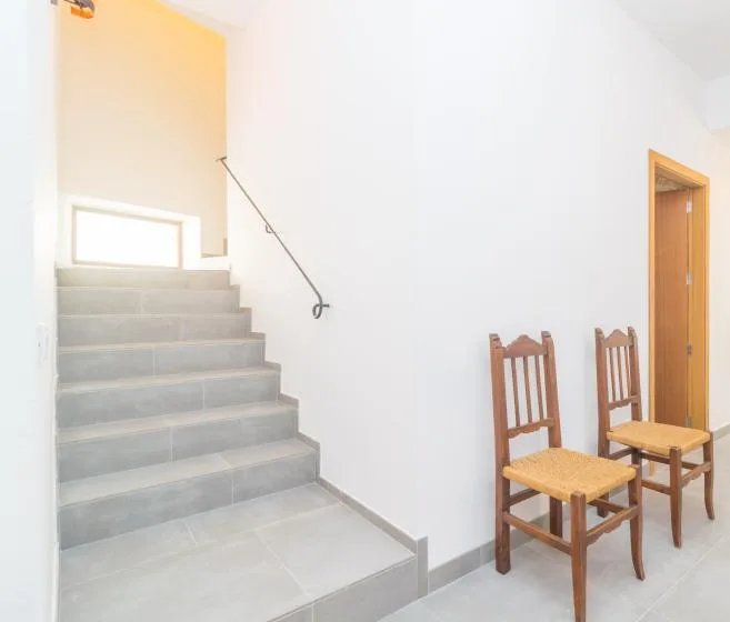 Una escalera sube junto a dos sillas de madera en un interior luminoso.