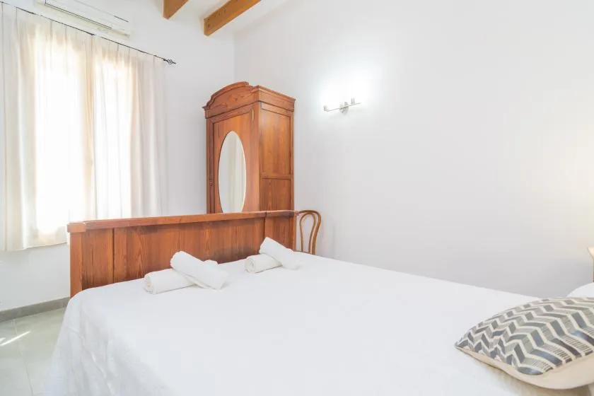 Un dormitorio luminoso con una cama y un armario de madera junto a una ventana con cortinas.