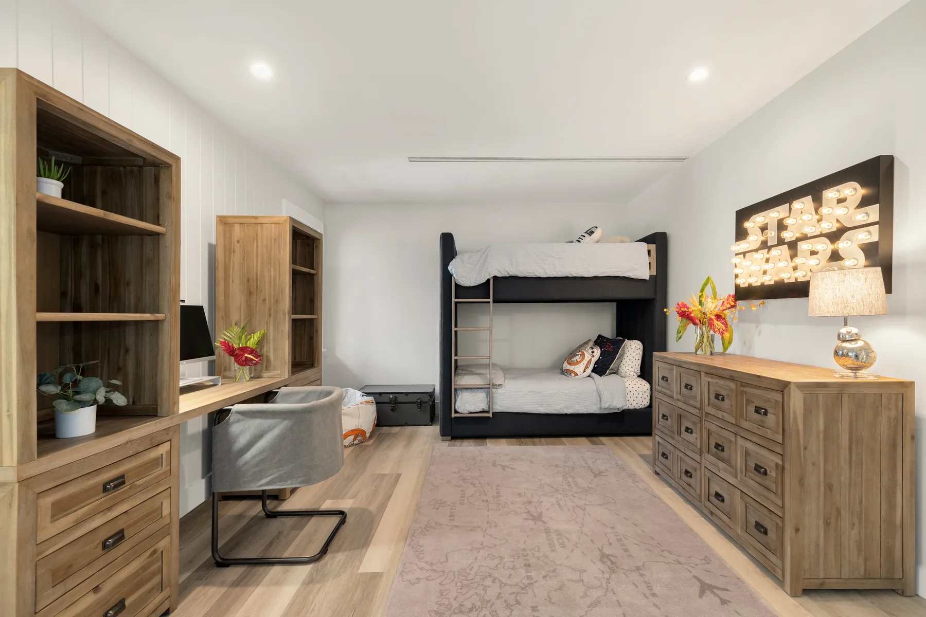 Un dormitorio luminoso con una litera, un escritorio y muebles de madera.