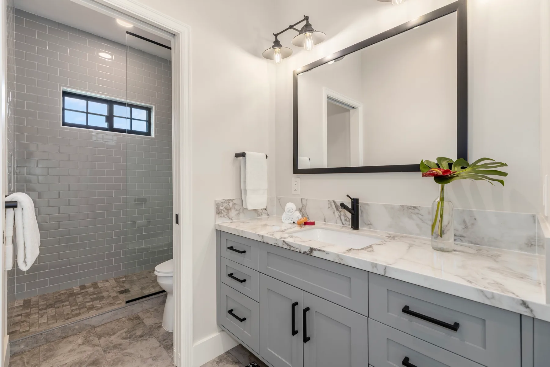 Baño con tocador gris, espejo grande y ducha de vidrio.