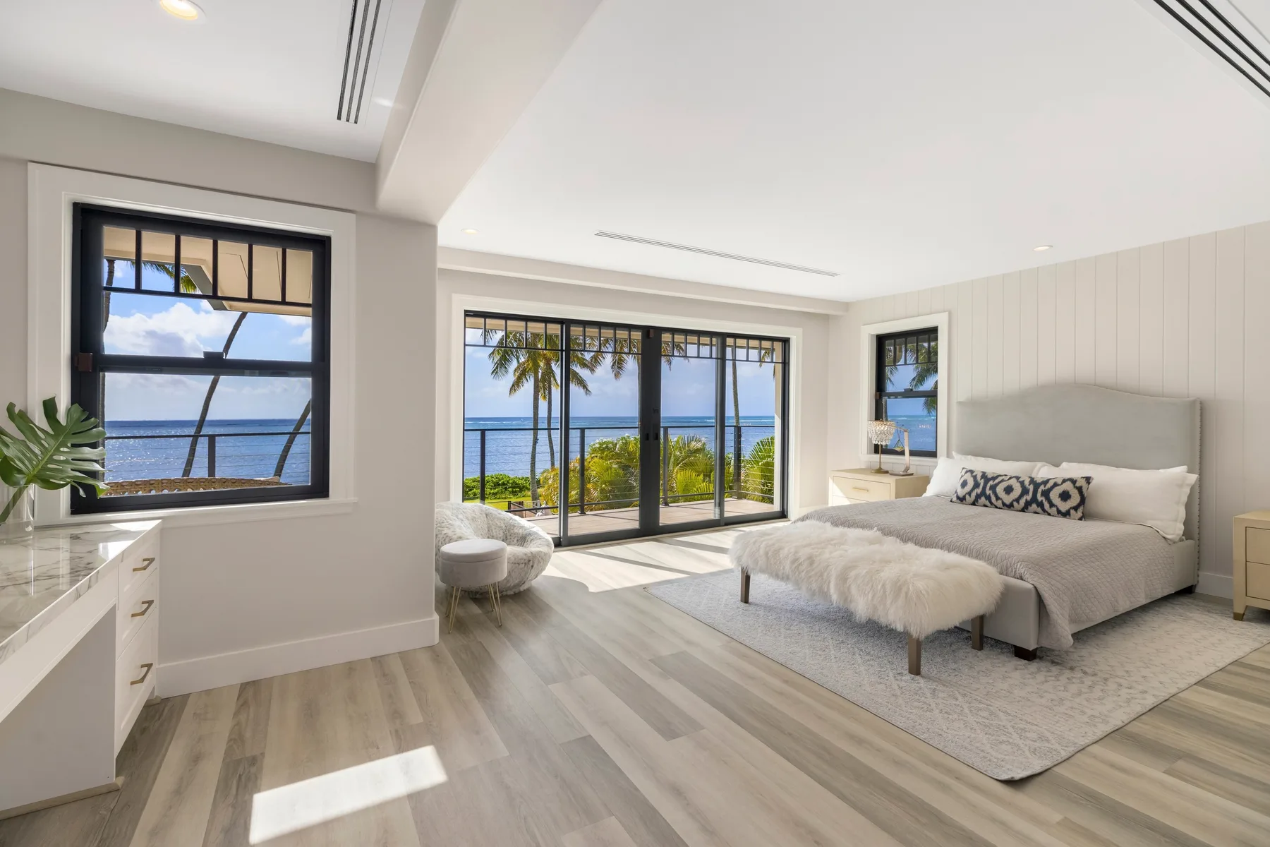 Un dormitorio luminoso con una cama junto a grandes ventanales con vistas al mar.