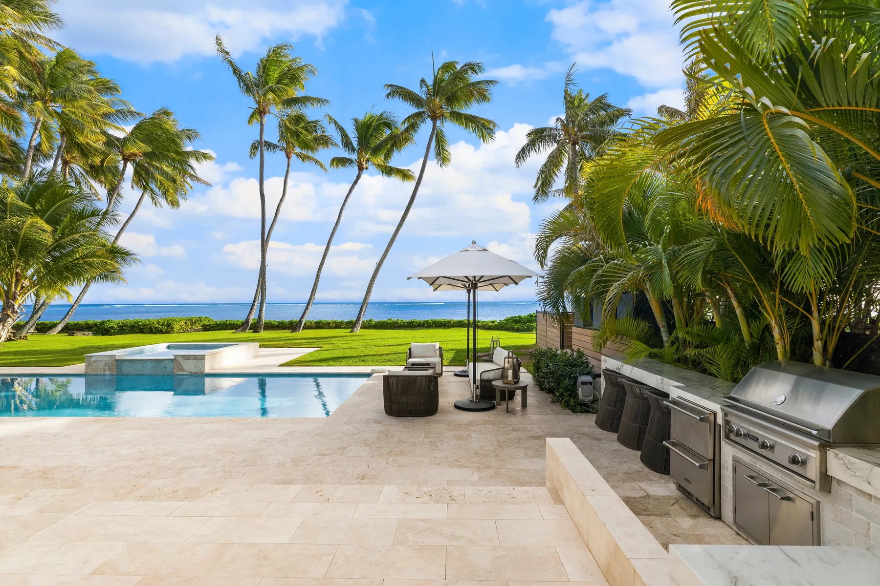 Un patio junto a la piscina mira al océano, con palmeras y asientos al aire libre.