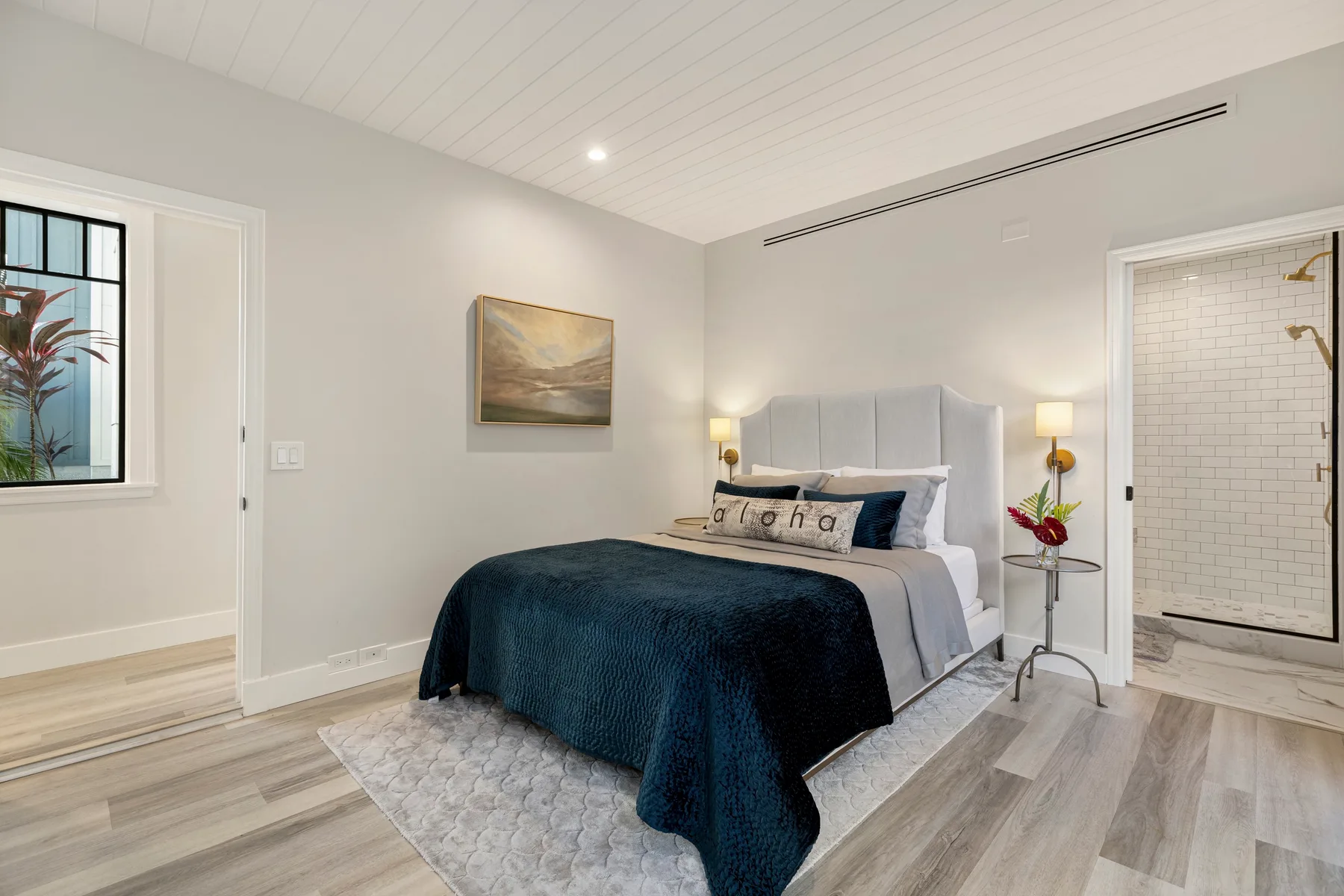 Un dormitorio luminoso con una cama, mesitas de noche y una zona de ducha contigua.