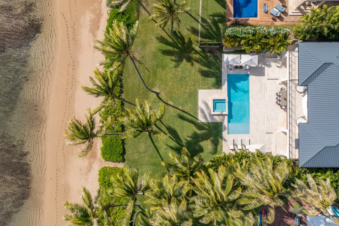 Una vista aérea muestra una propiedad junto a la playa con piscina y palmeras.