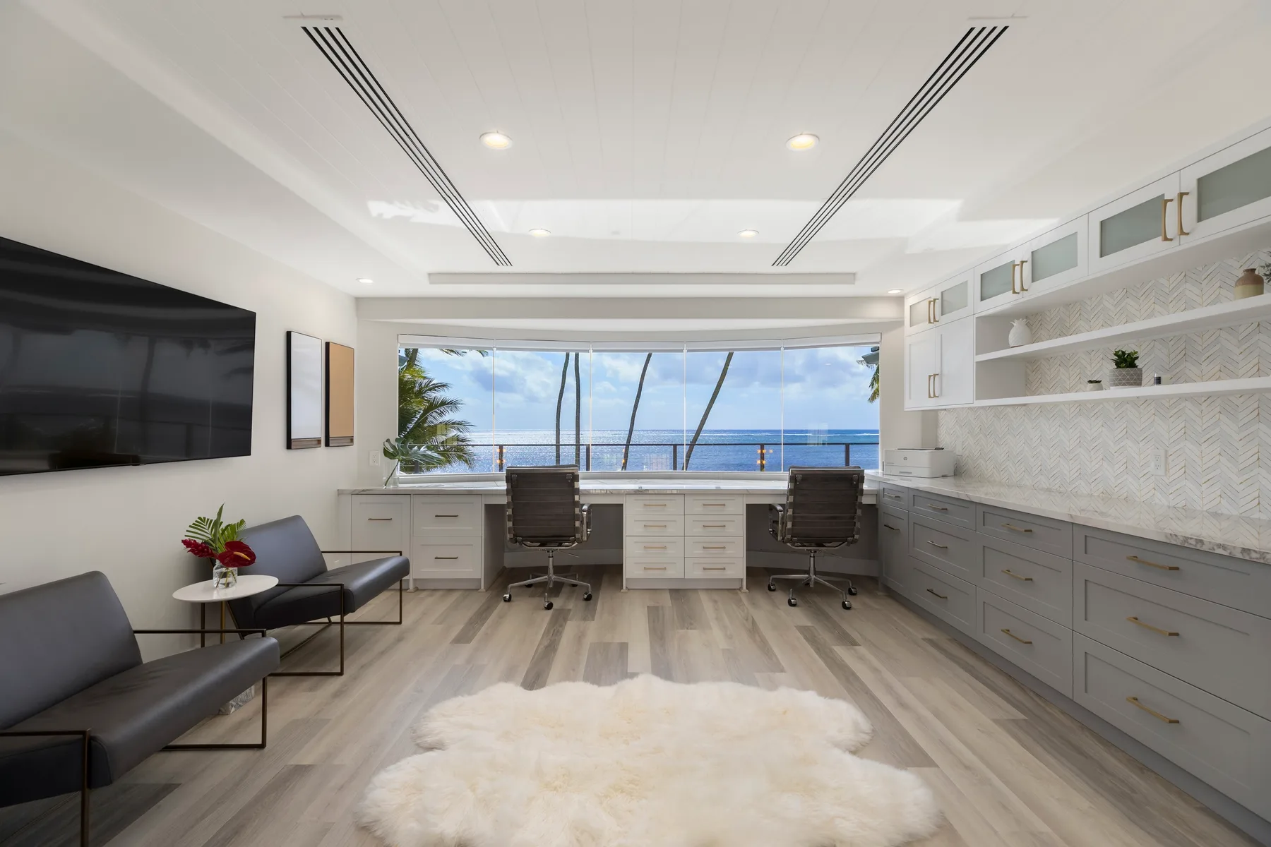 Una oficina luminosa con escritorios empotrados y asientos frente a una gran ventana con vista al mar.