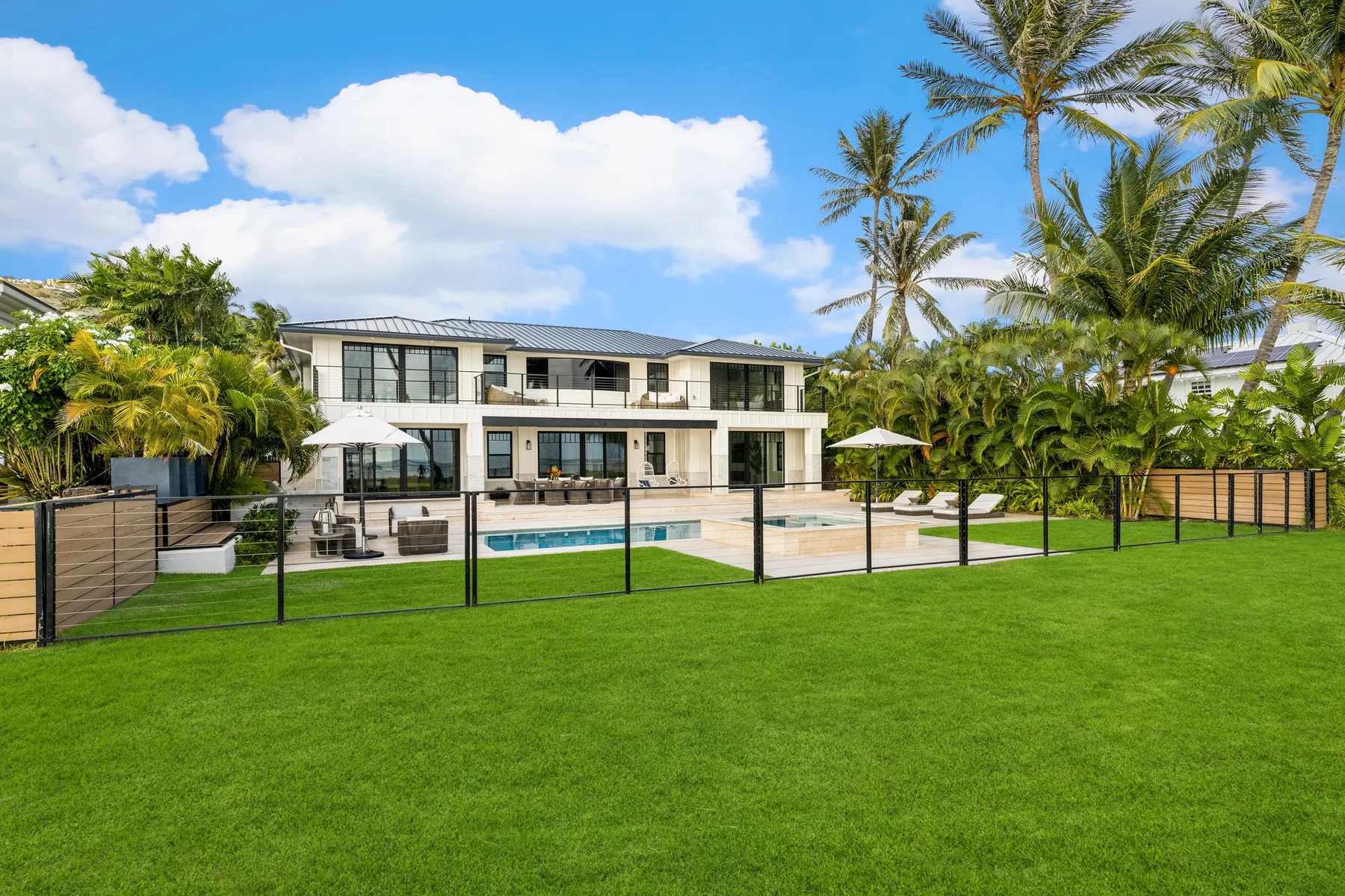 Una casa moderna se alza detrás de una piscina cercada y un césped verde.
