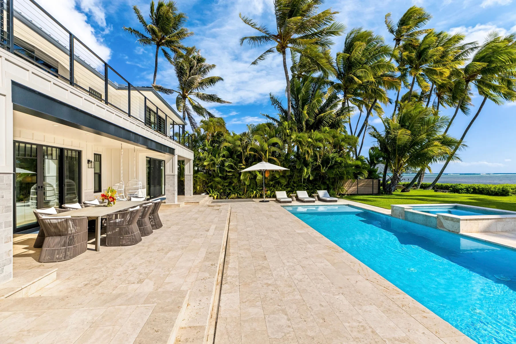 Un patio junto a la piscina con asientos al aire libre, palmeras y vista al mar.