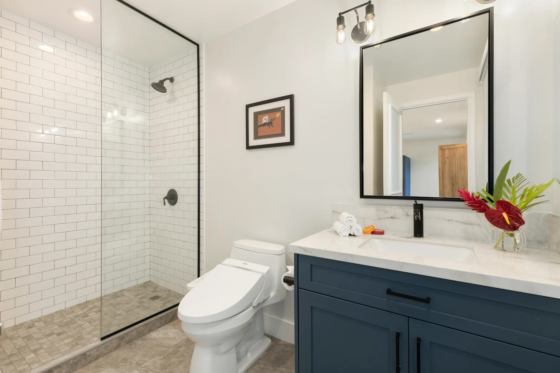Un baño con ducha de vidrio, inodoro y tocador azul oscuro.