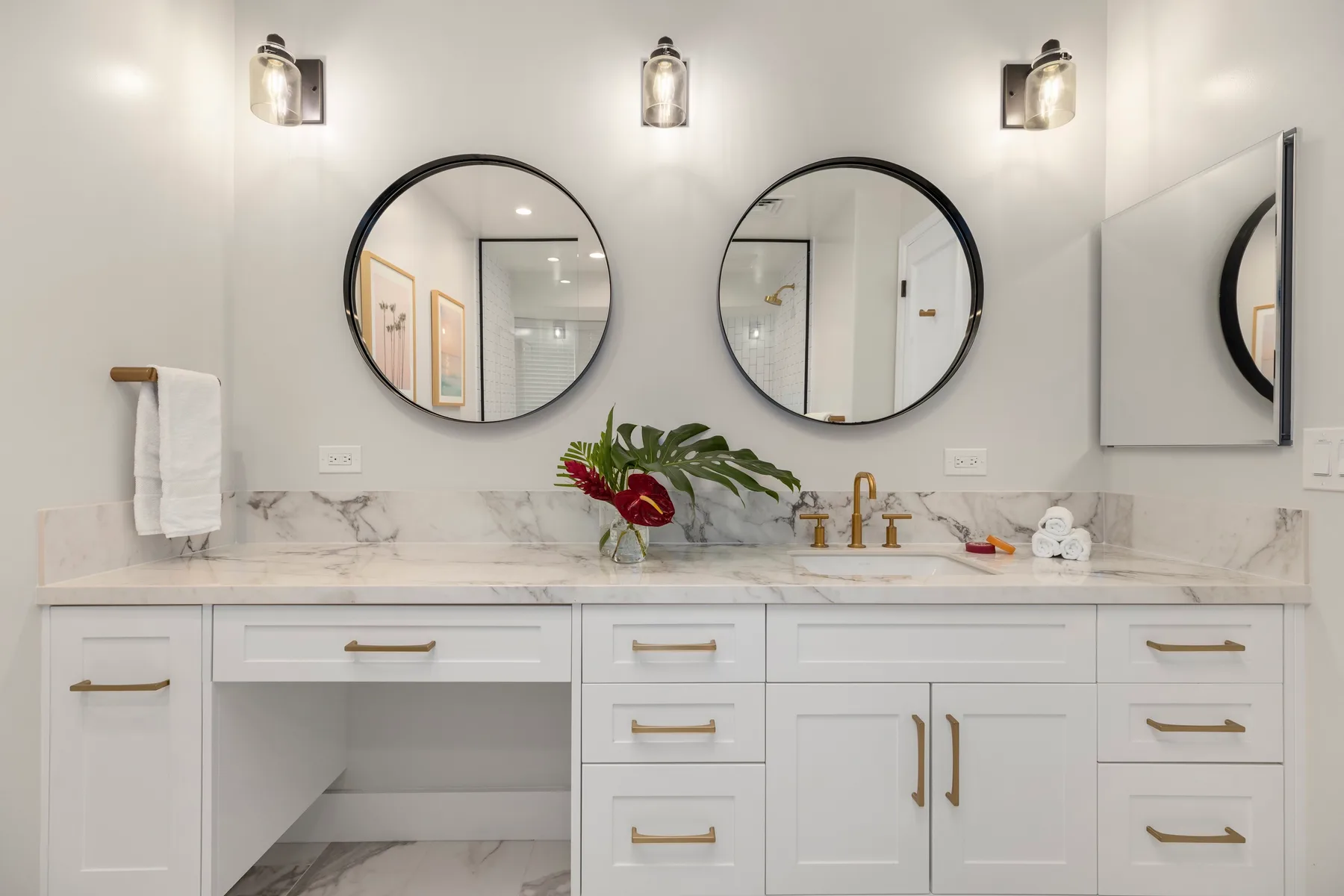 Un tocador de baño luminoso con espejos redondos y un arreglo floral.