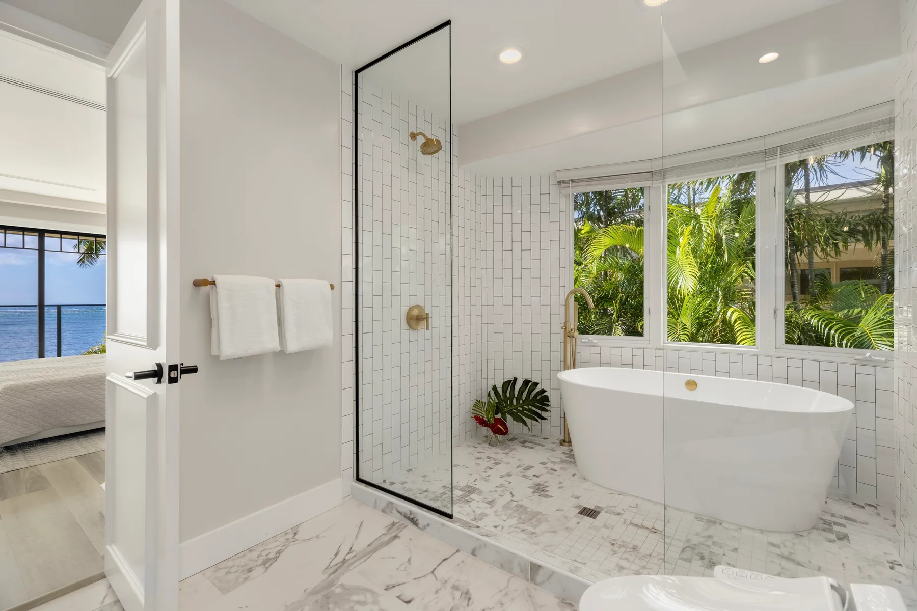 Un baño luminoso con bañera exenta, ducha de vidrio y ventanas con vistas a la vegetación.