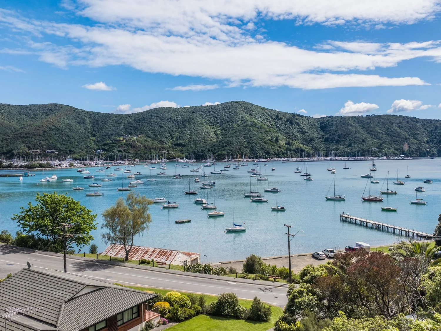 Boats are moored across a bay beneath green hills and a partly cloudy sky.