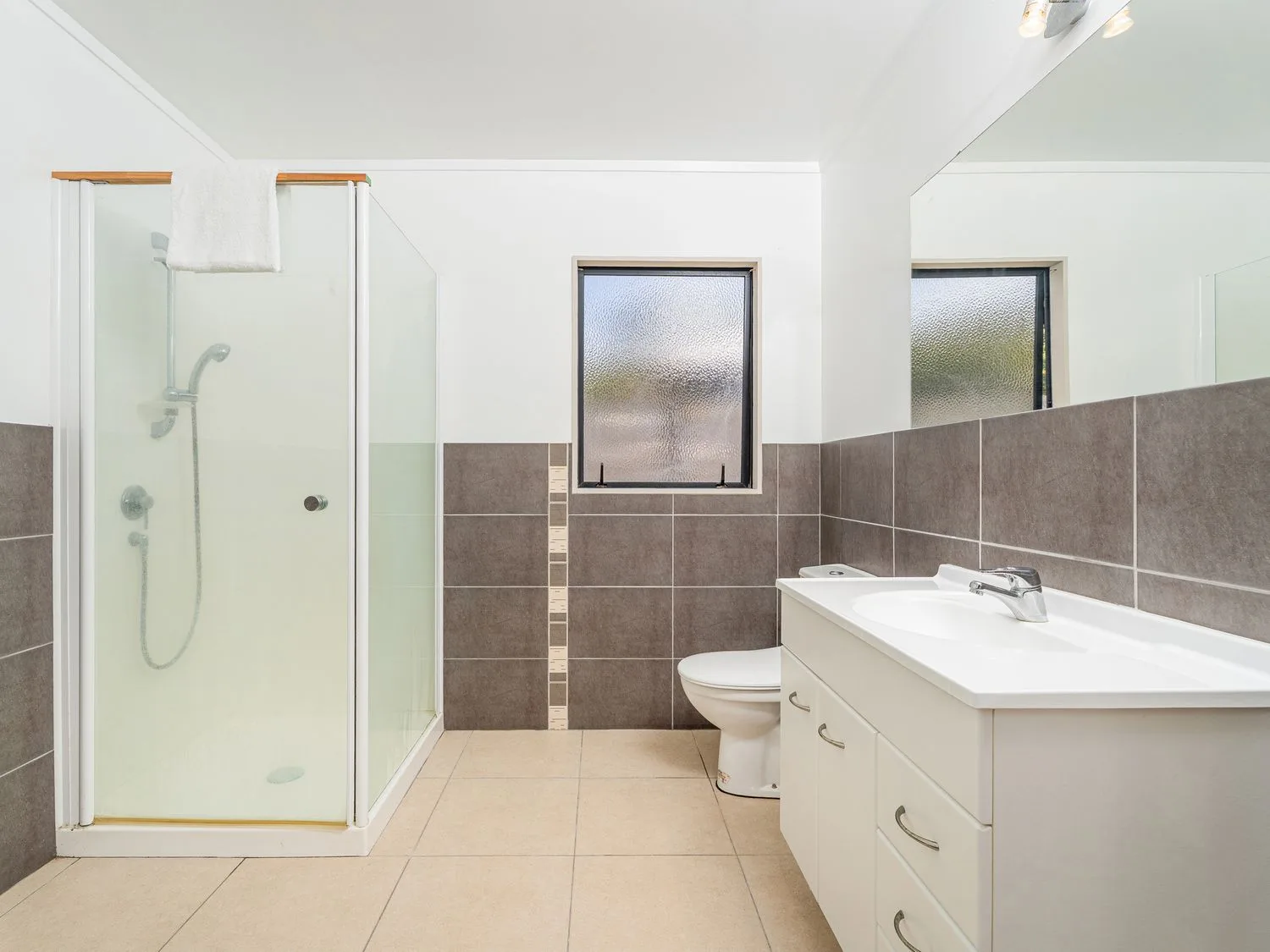 A bathroom with a shower, toilet, and vanity beside tiled walls.