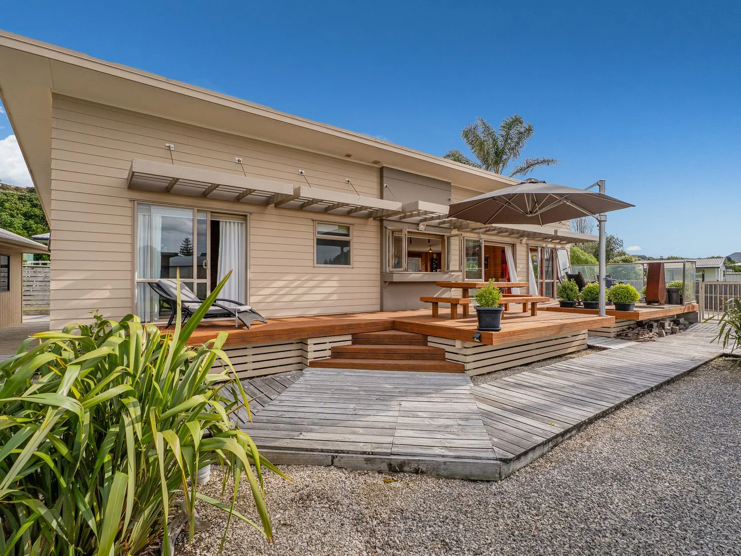 A wooden deck beside a house, with outdoor seating and a large umbrella.