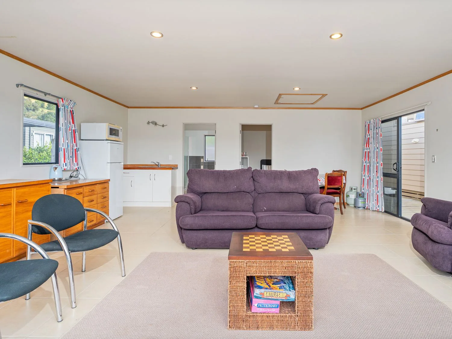 A living room with purple seating, a low table, and a kitchen area.
