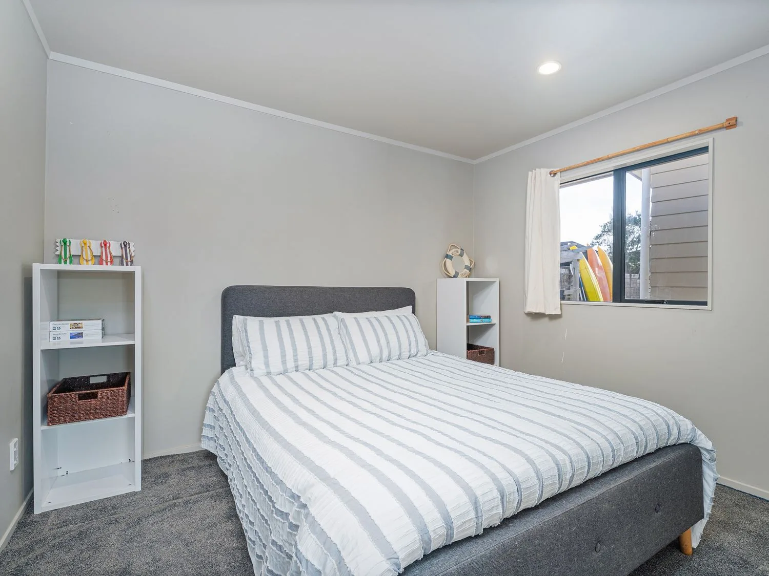 A bedroom with a striped bed and shelving beside a window.