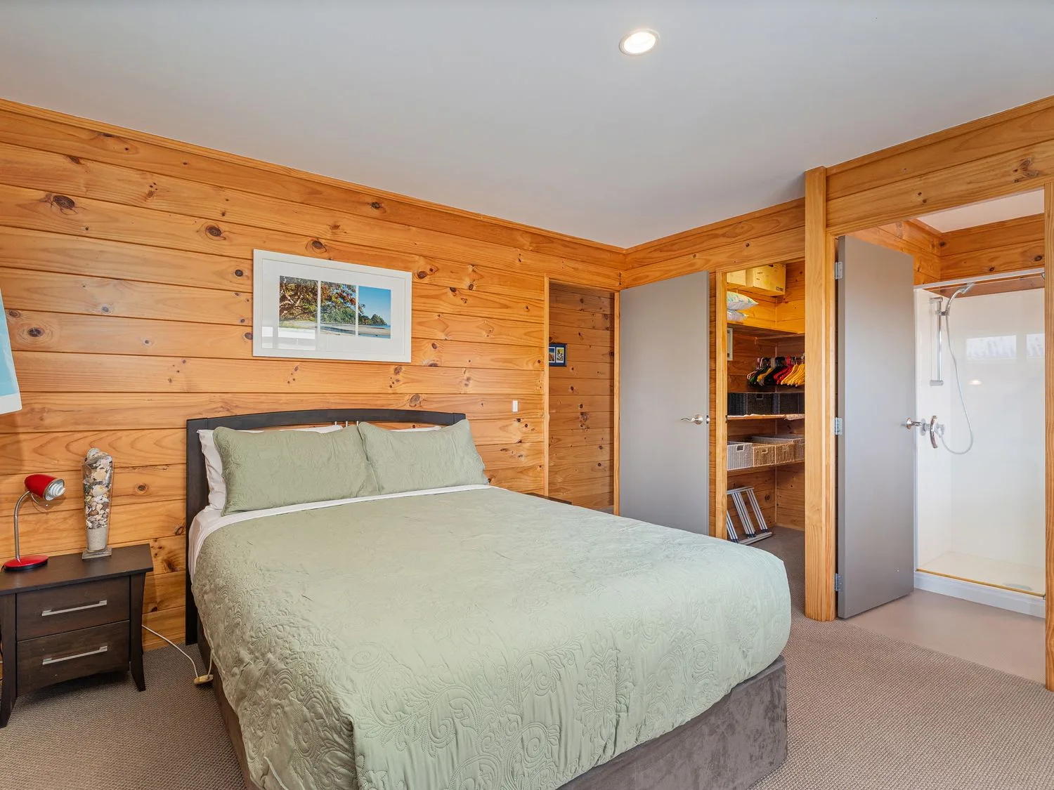 A bedroom with a bed, bedside table, and an open closet beside the bathroom.
