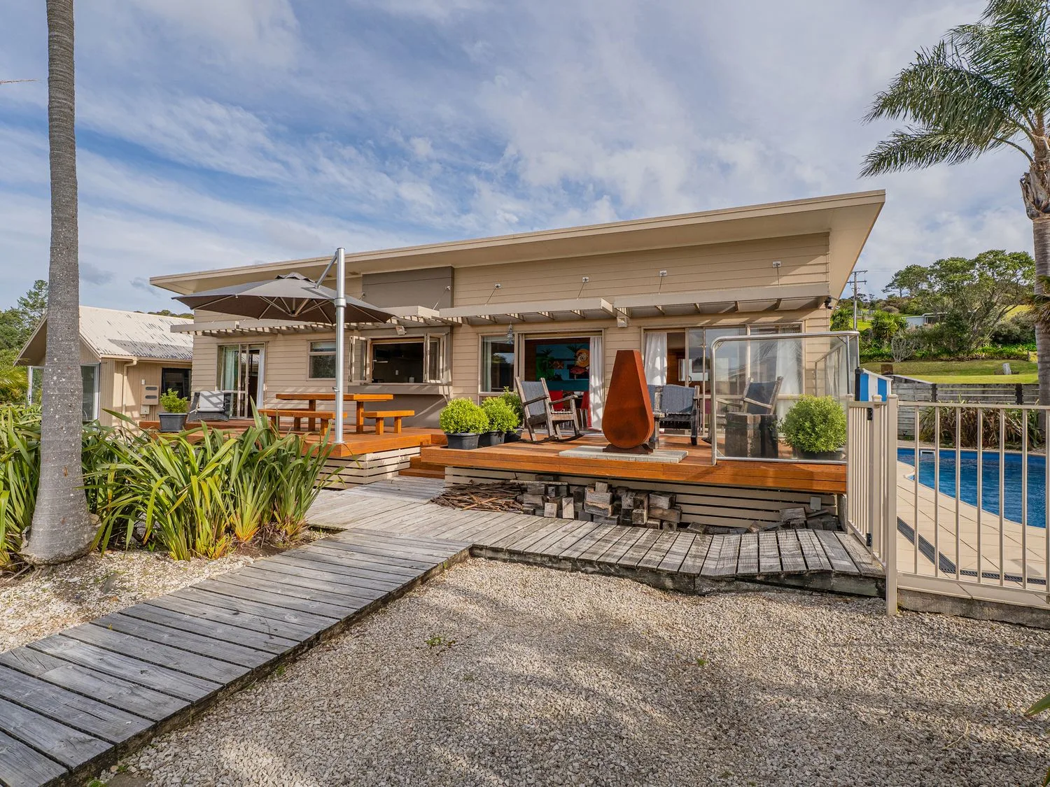 A modern house opens onto a wooden deck with outdoor seating and a pool.