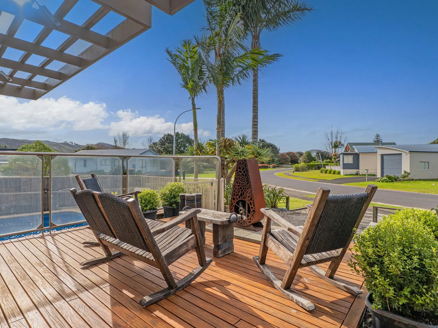 An outdoor deck has wooden seating beside a glass railing and landscaped grounds.