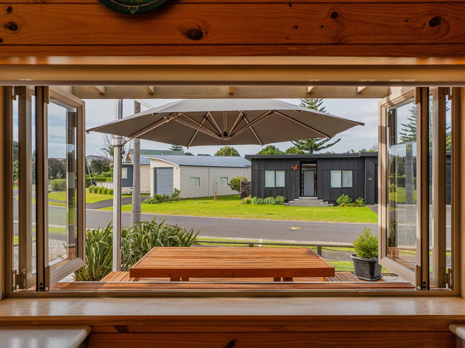 An open window frames an outdoor table and umbrella overlooking a lawn and nearby buildings.