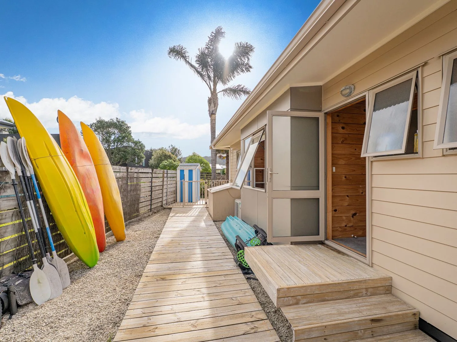 An outdoor walkway leads to a house entrance, with colorful kayaks beside it.