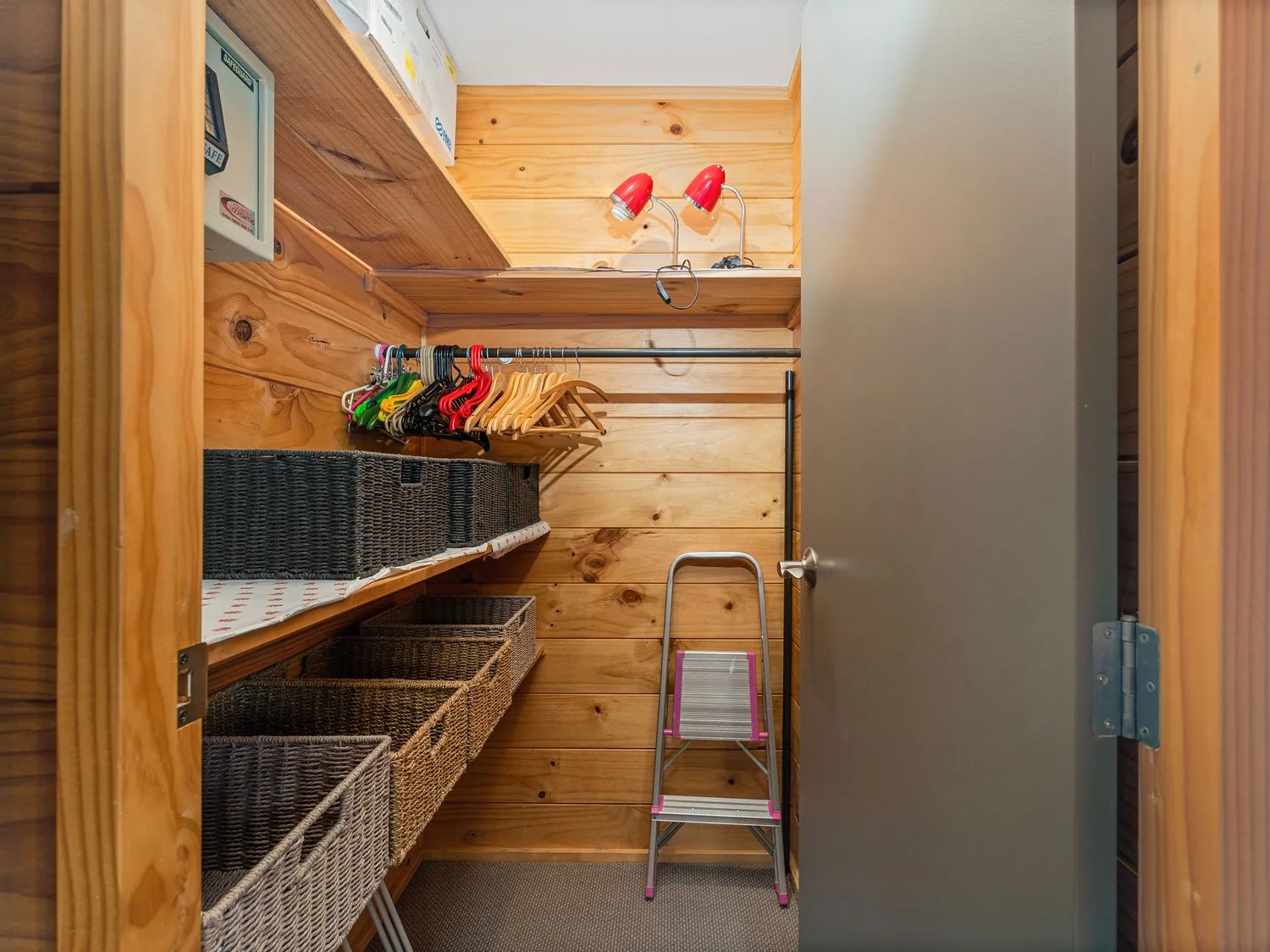 A wooden closet with shelves, storage baskets, and hanging clothes.