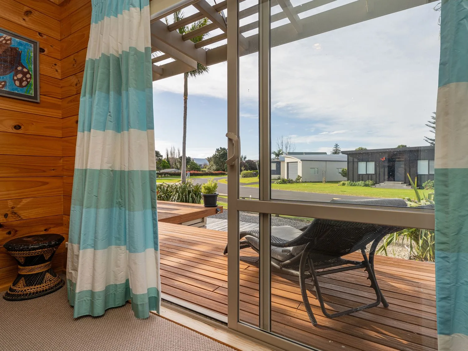 A living room with a view of a deck and garden at Whangapoua