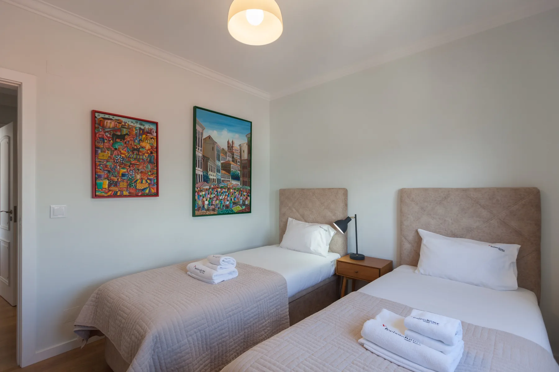 Un dormitorio con dos camas, cuadros coloridos y toallas dobladas.
