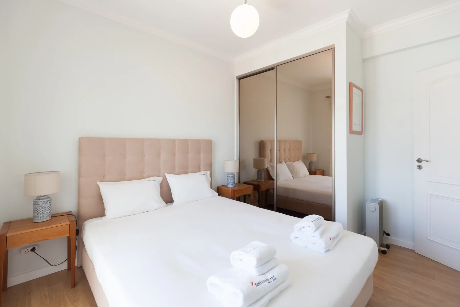 Un dormitorio con una cama doble, mesitas de noche y puertas de armario espejadas.