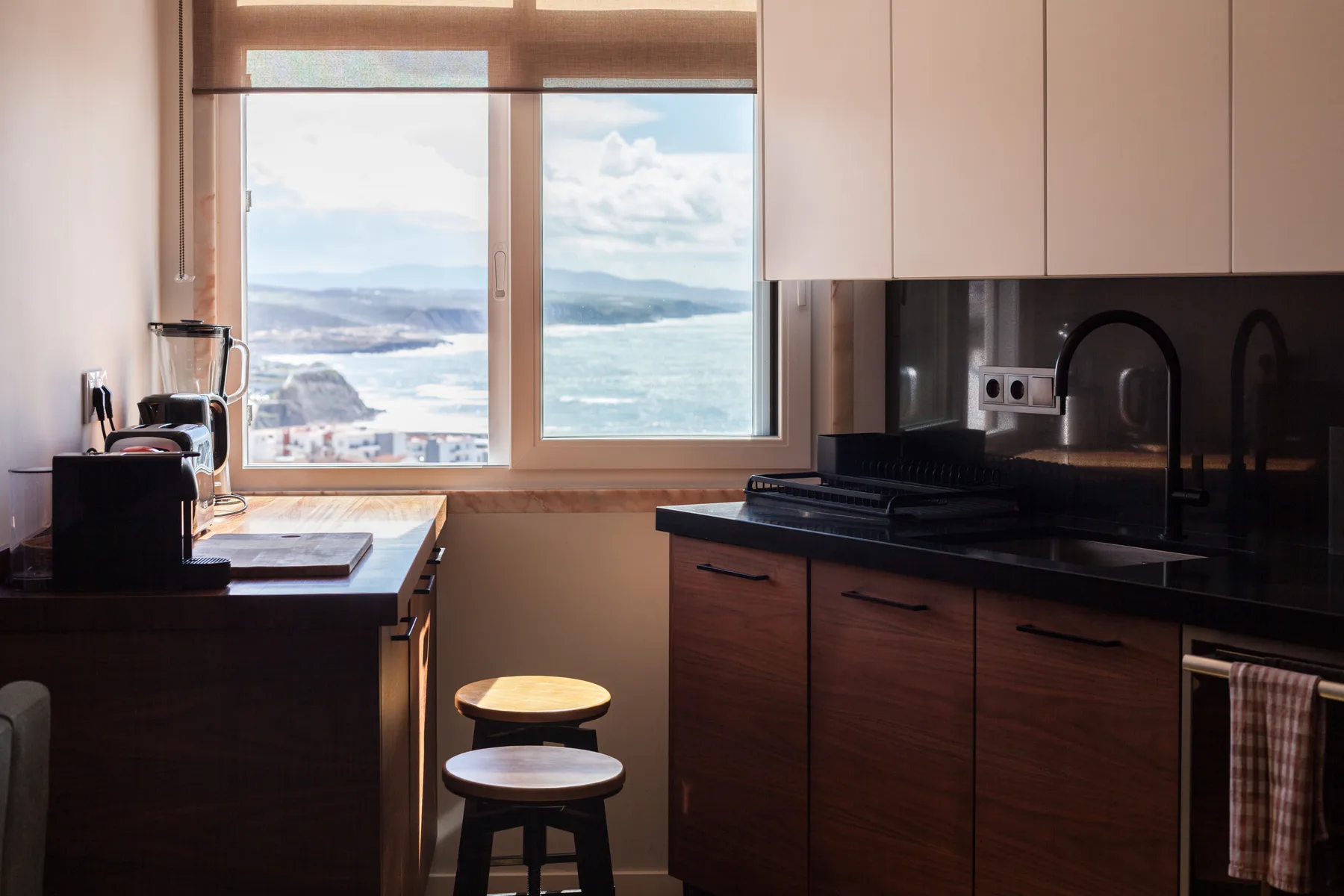 Una cocina moderna con encimeras oscuras y una ventana amplia con vistas al mar.