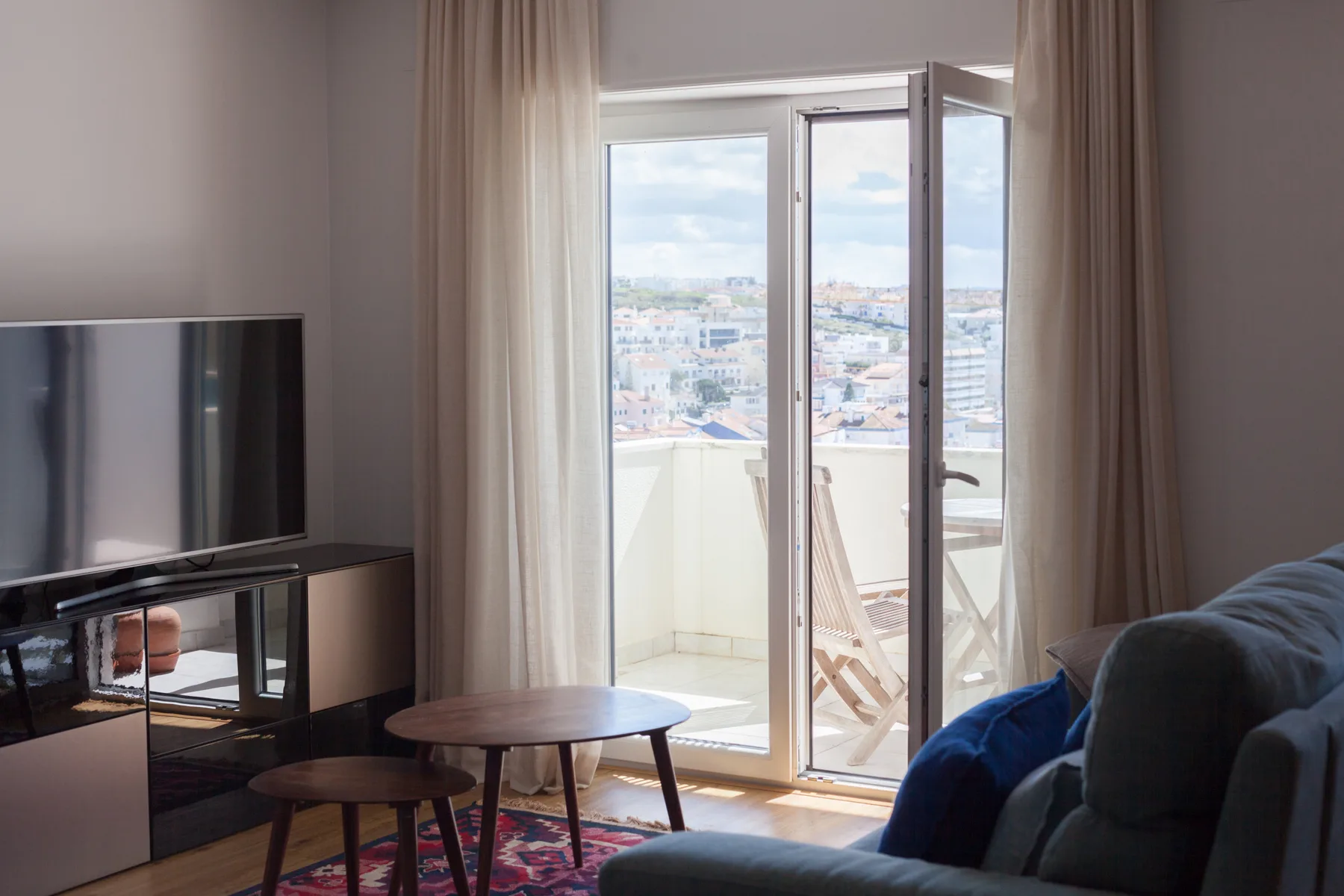 Un salón se abre a un balcón, con edificios de la ciudad a la vista.