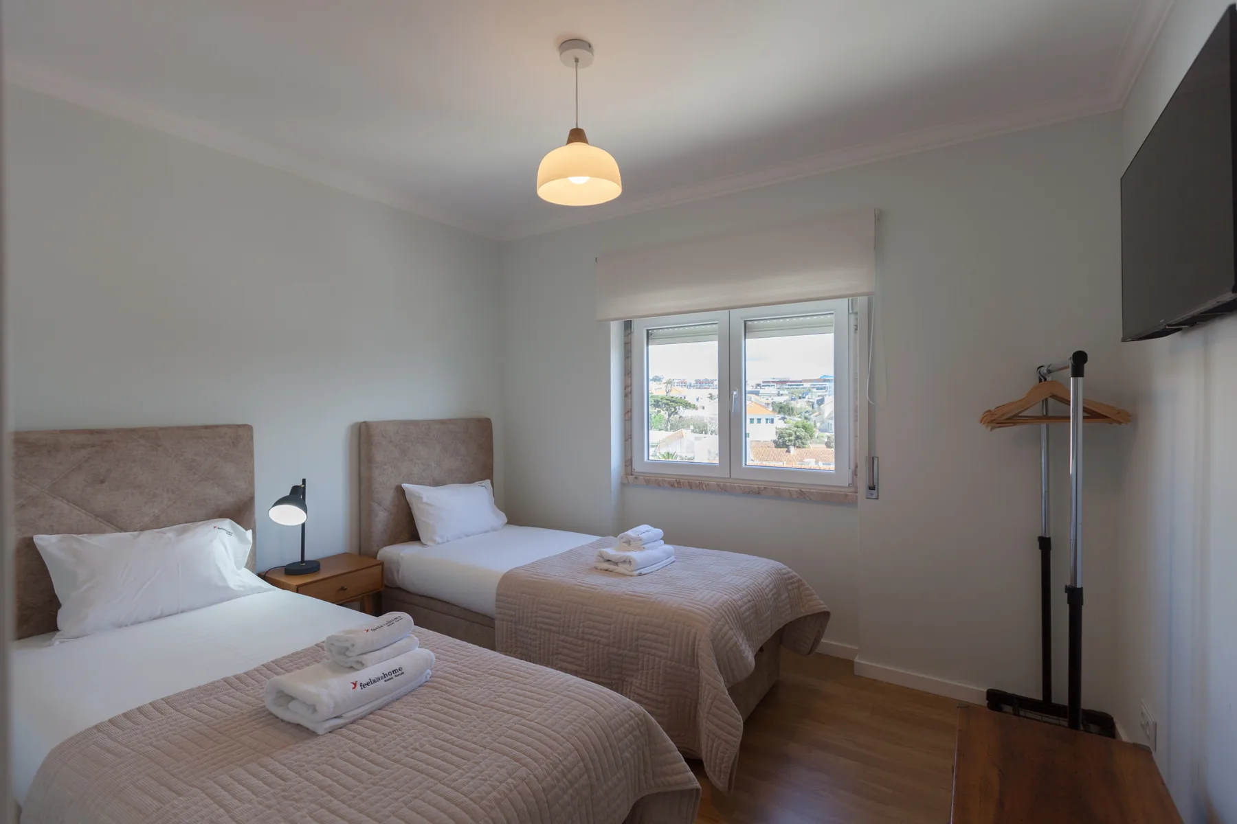 Un dormitorio con dos camas y una ventana con vistas a edificios cercanos.