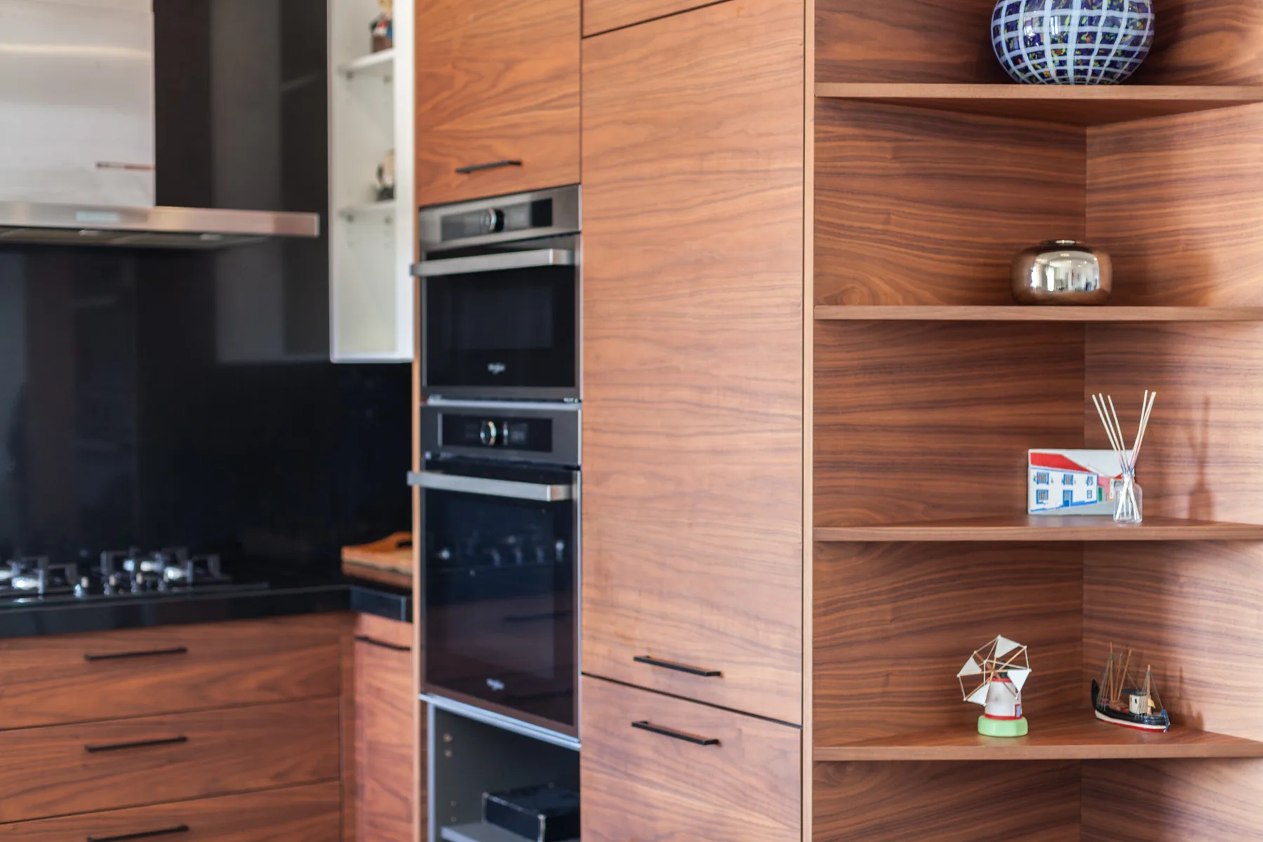 Una cocina moderna con armarios de madera, hornos integrados y estantes abiertos.