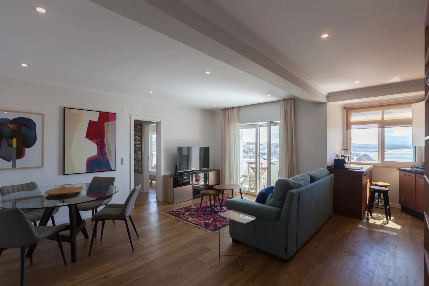 Sala de estar y comedor con asientos, un televisor y grandes ventanas.