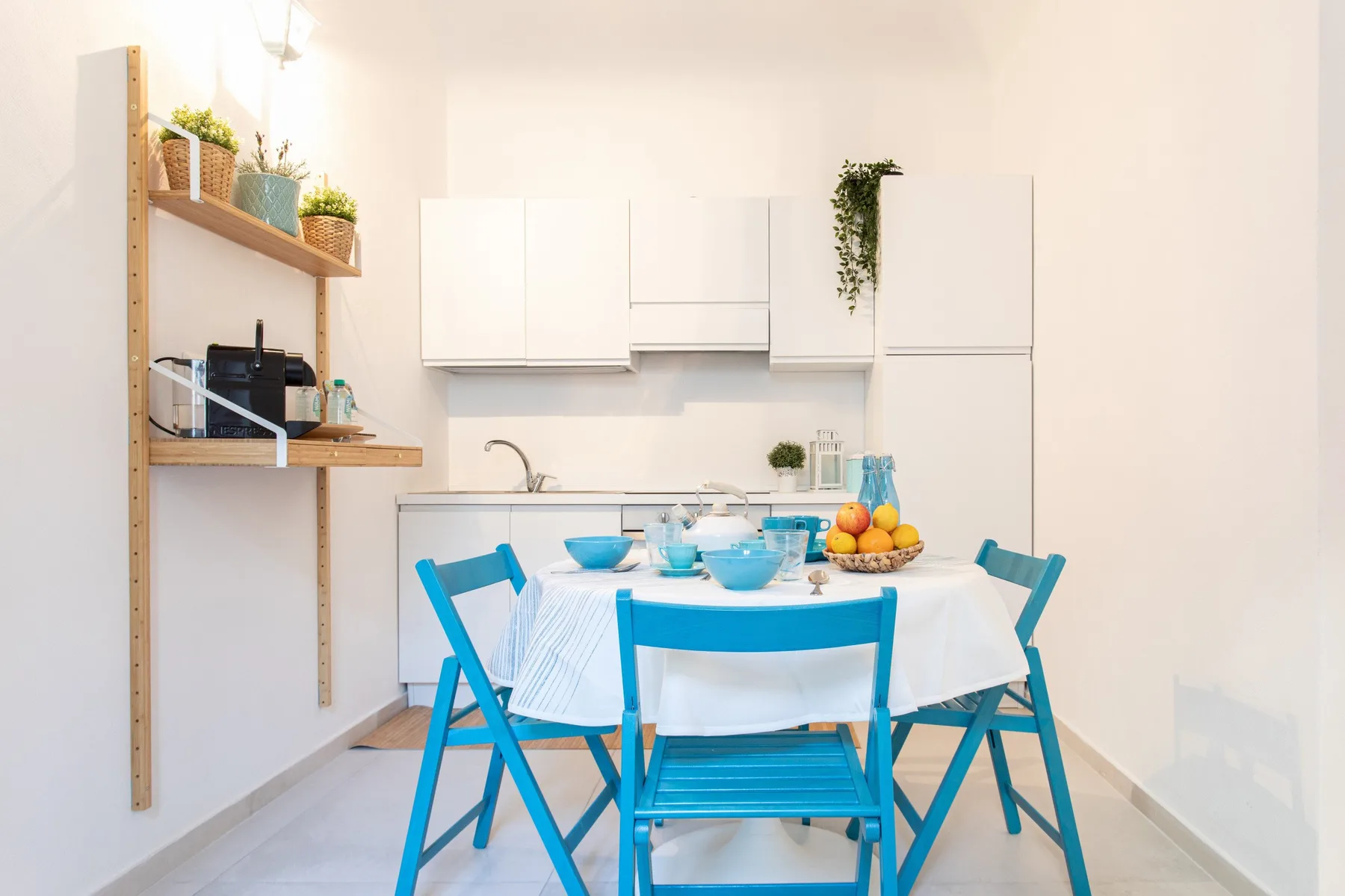 A bright dining area with blue seating around a table set with dishes and fruit.