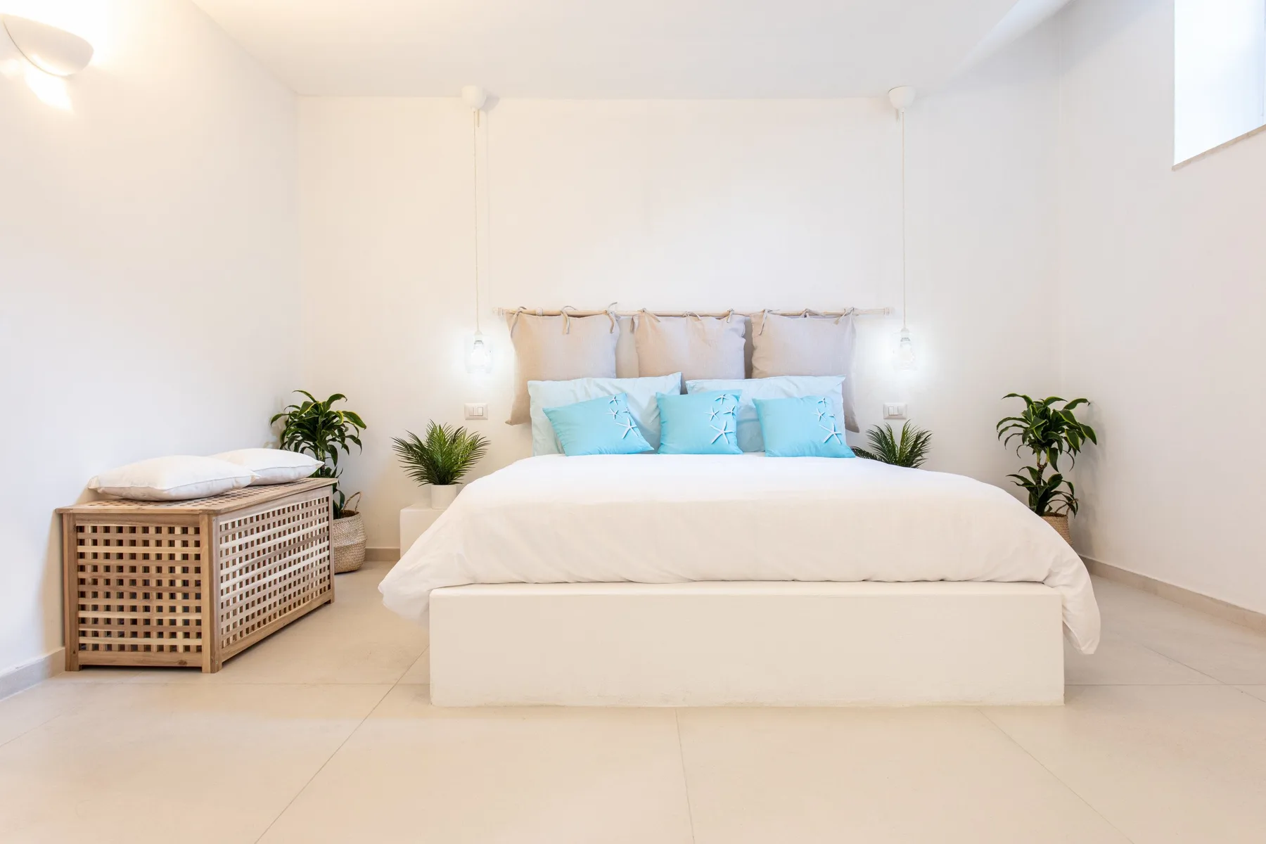 A bright bedroom with a white bed, blue pillows, and green plants.