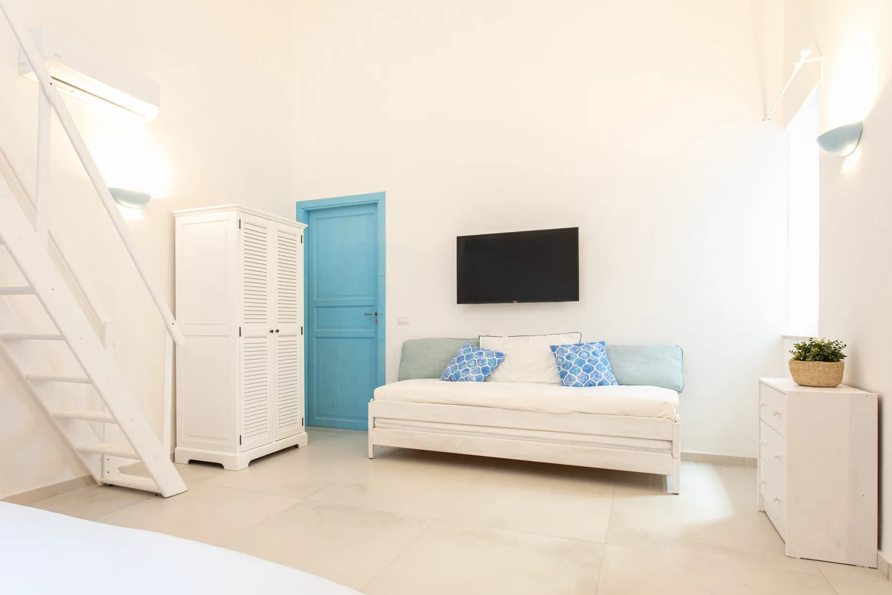 Una sala luminosa con un sofá blanco debajo de un televisor montado en la pared.