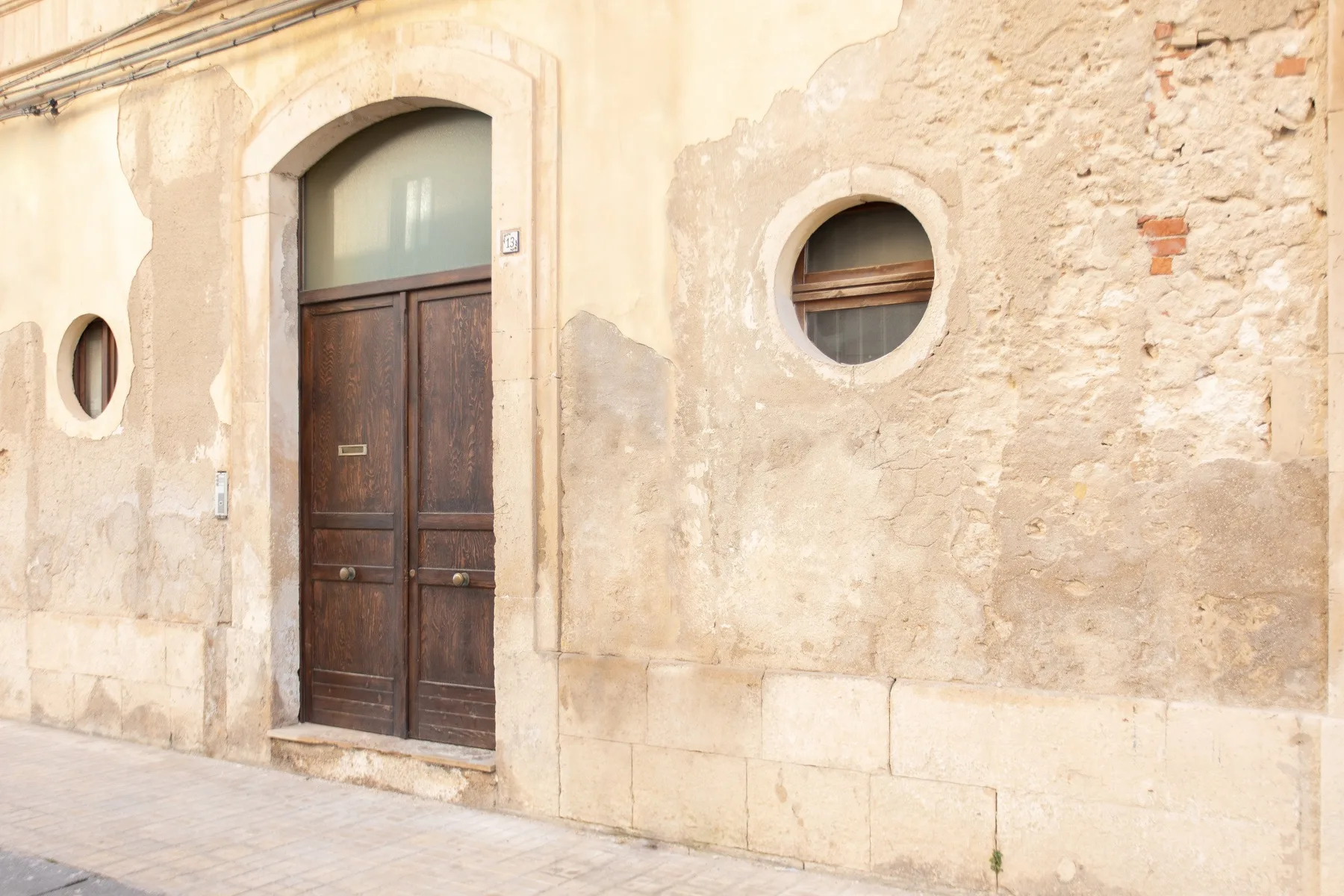 A weathered exterior wall has a dark wooden door and round windows.