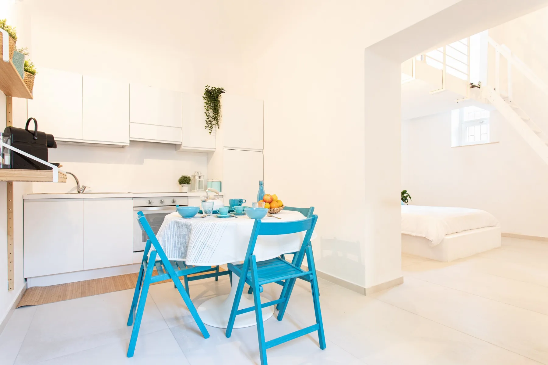 A bright dining area with a turquoise table and chairs beside a white kitchen.