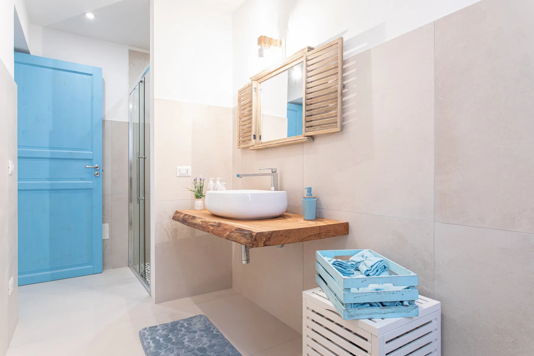 A bright bathroom with a blue door, wall mirror, and wooden vanity.